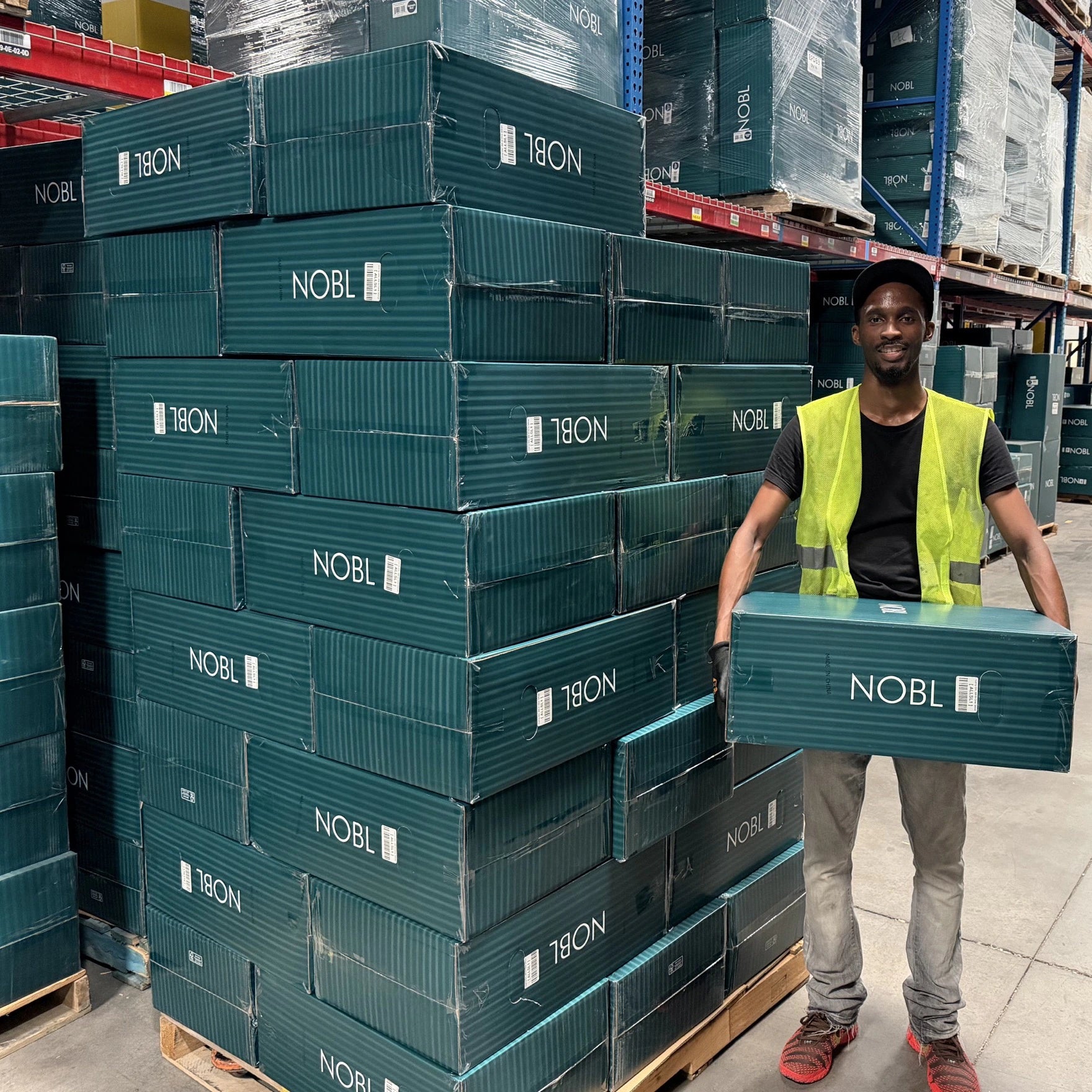 NOBL warehouse team member holding a suitcase box beside stacked luggage